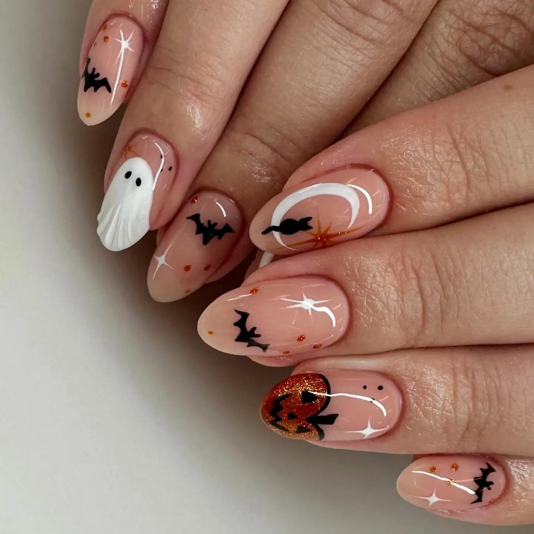 Halloween press-on nails with bats, ghost, pumpkin, and glittery accents on nude base