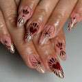 Hand with almond-shaped press-on nails featuring red hearts, gold foil, and star designs