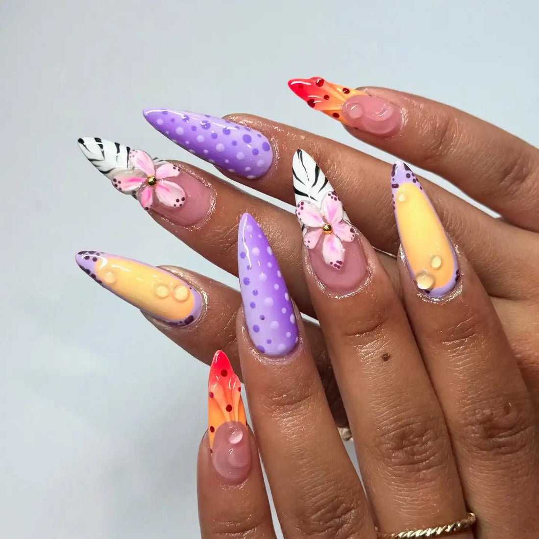 Hand with long press-on nails in pastel purple, yellow, floral and polka dot nail art.