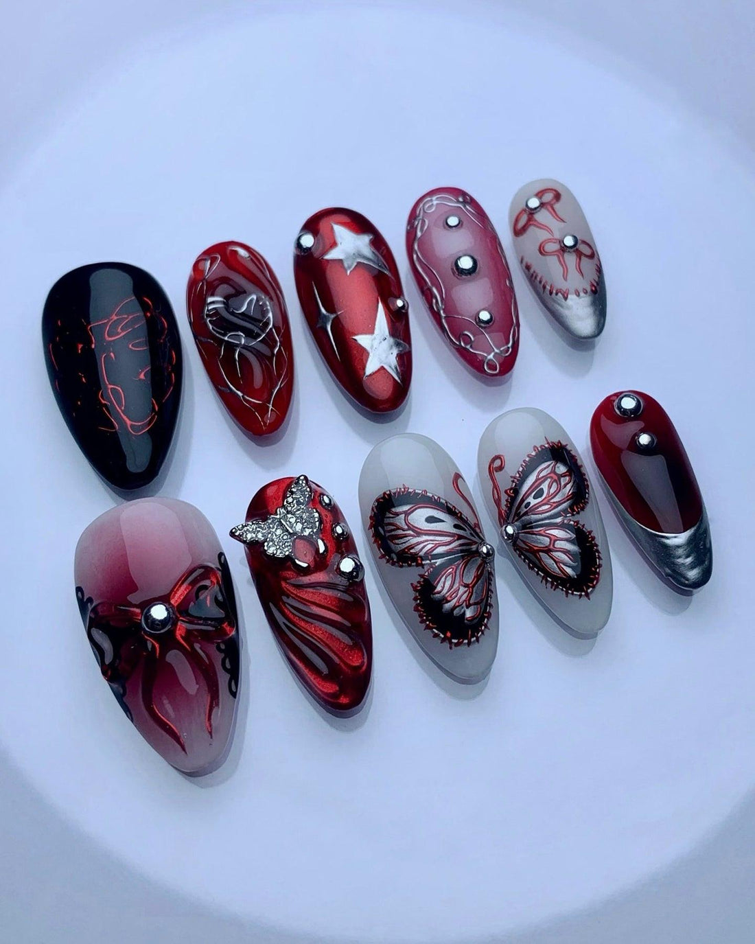 Set of handmade press-on nails in red, black, and silver with butterfly, star, and rhinestone designs