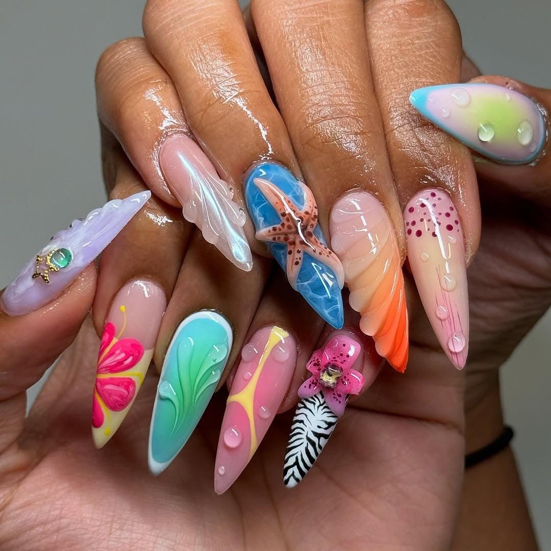 Hand with long, colorful, custom press-on nails featuring 3D art, tropical and floral designs.
