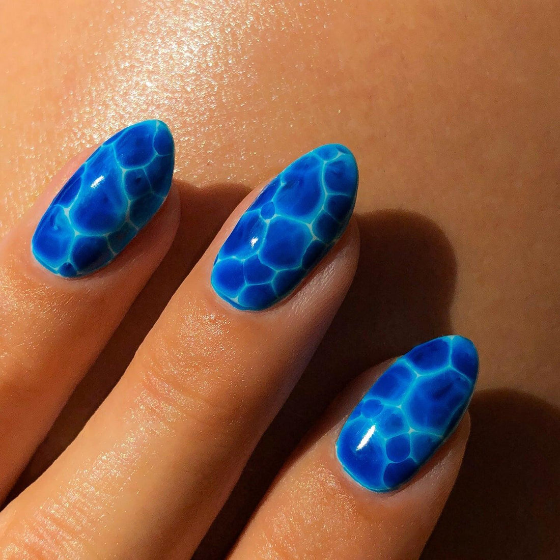 Hand with custom blue press-on nails featuring a water ripple design in sunlight
