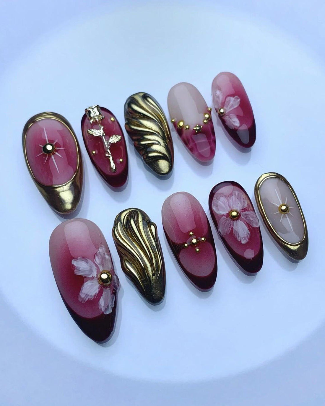 Handmade press-on nails in burgundy and gold with floral and metallic designs