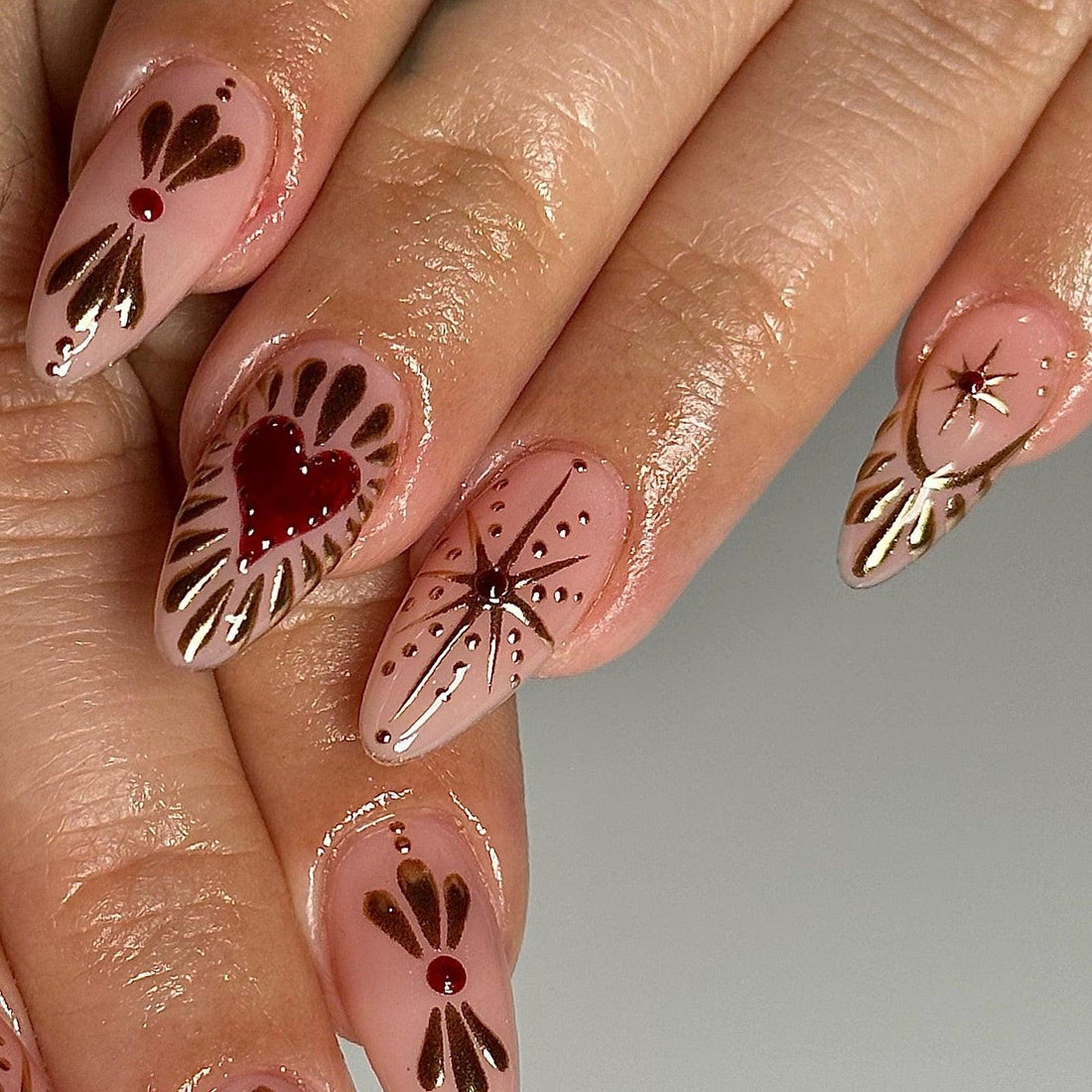 Hand with almond-shaped press-on nails featuring red hearts, gold foil, and star designs