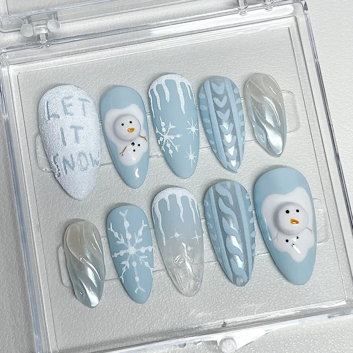 Winter-themed press-on nails with snowman designs, snowflakes, icicle patterns, and 'Let it Snow' text.