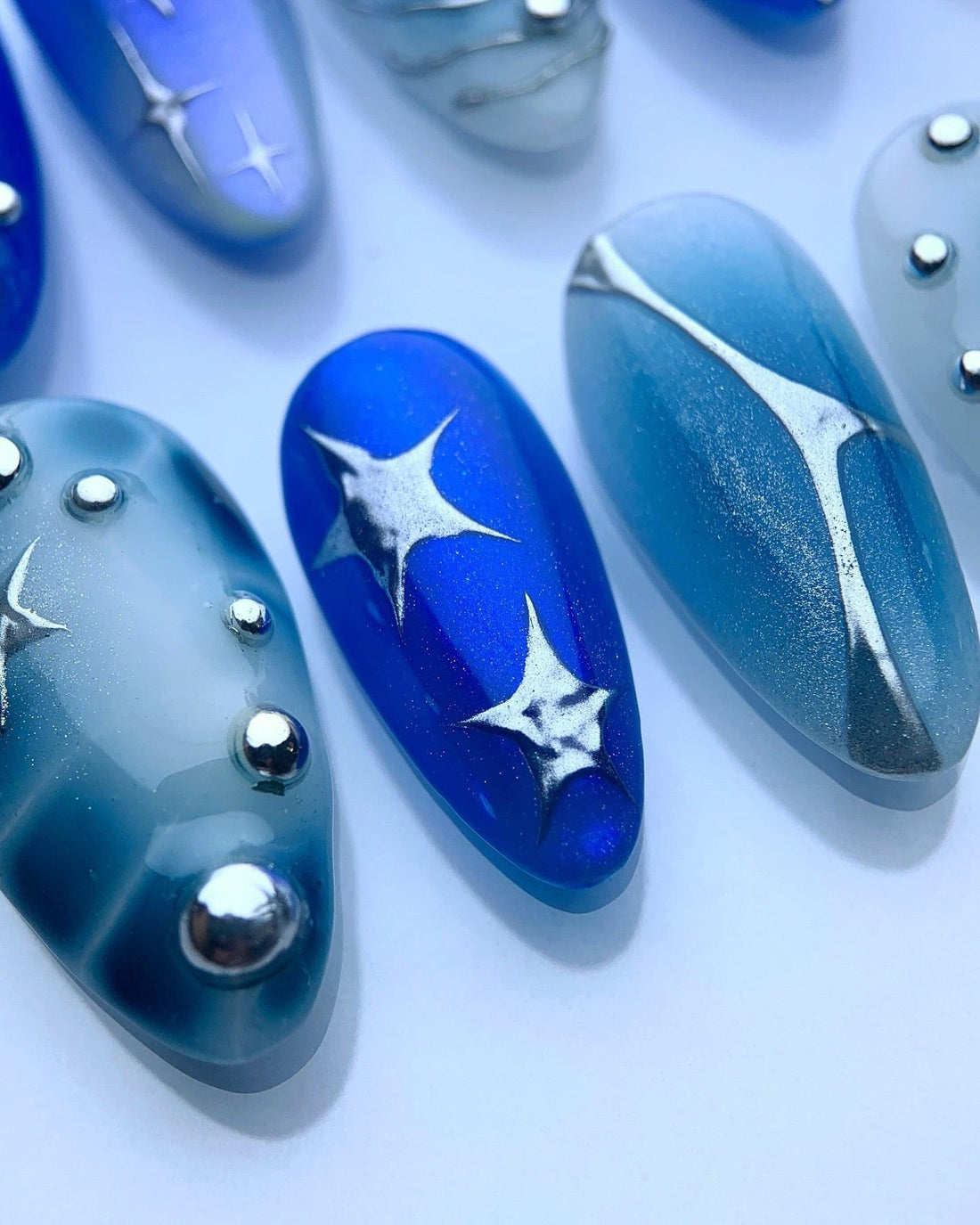 Blue and silver press-on nails with star and swirl designs, metallic accents, and gemstones