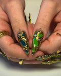 Handmade press-on nails with gold, green, and blue gemstone accents, stiletto shape