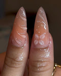 Handmade nude stiletto press-on nails with 3D swirl and floral designs, glossy finish