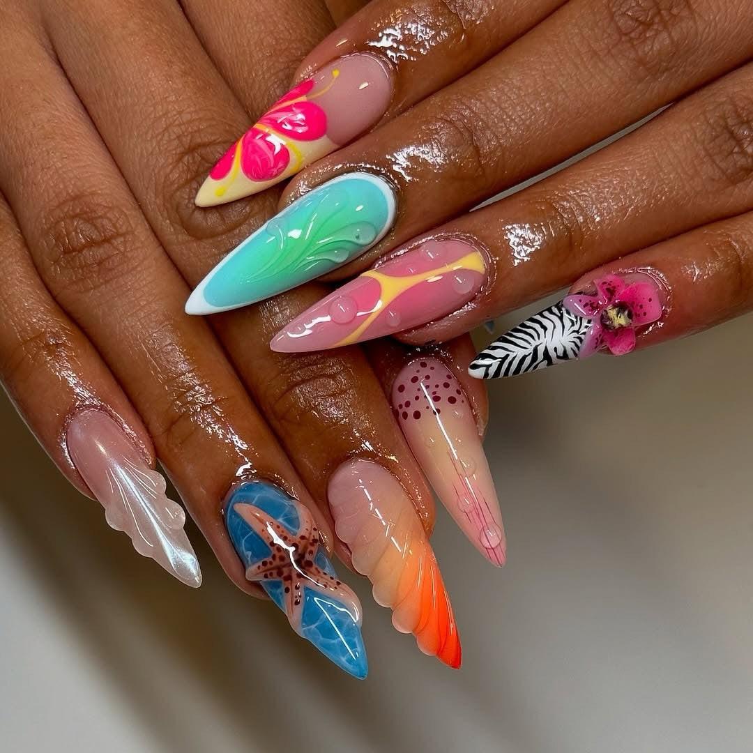 Hand with long, colorful, custom press-on nails featuring 3D art, tropical and floral designs.