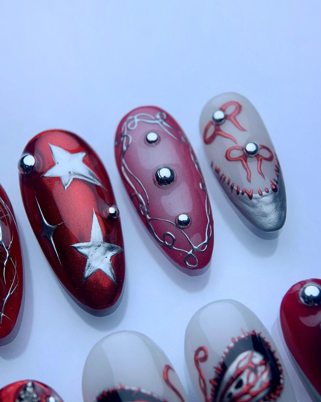 Set of handmade press-on nails in red, black, and silver with butterfly, star, and rhinestone designs