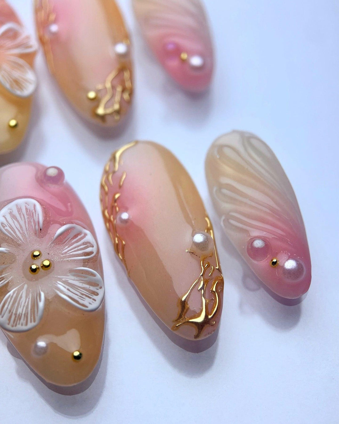 Handmade press-on nails with pink and nude ombre, gold accents, pearls, and floral designs.
