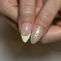Hand with press-on nails featuring 3D floral designs, pearls, light yellow French tips, and rhinestone accents.