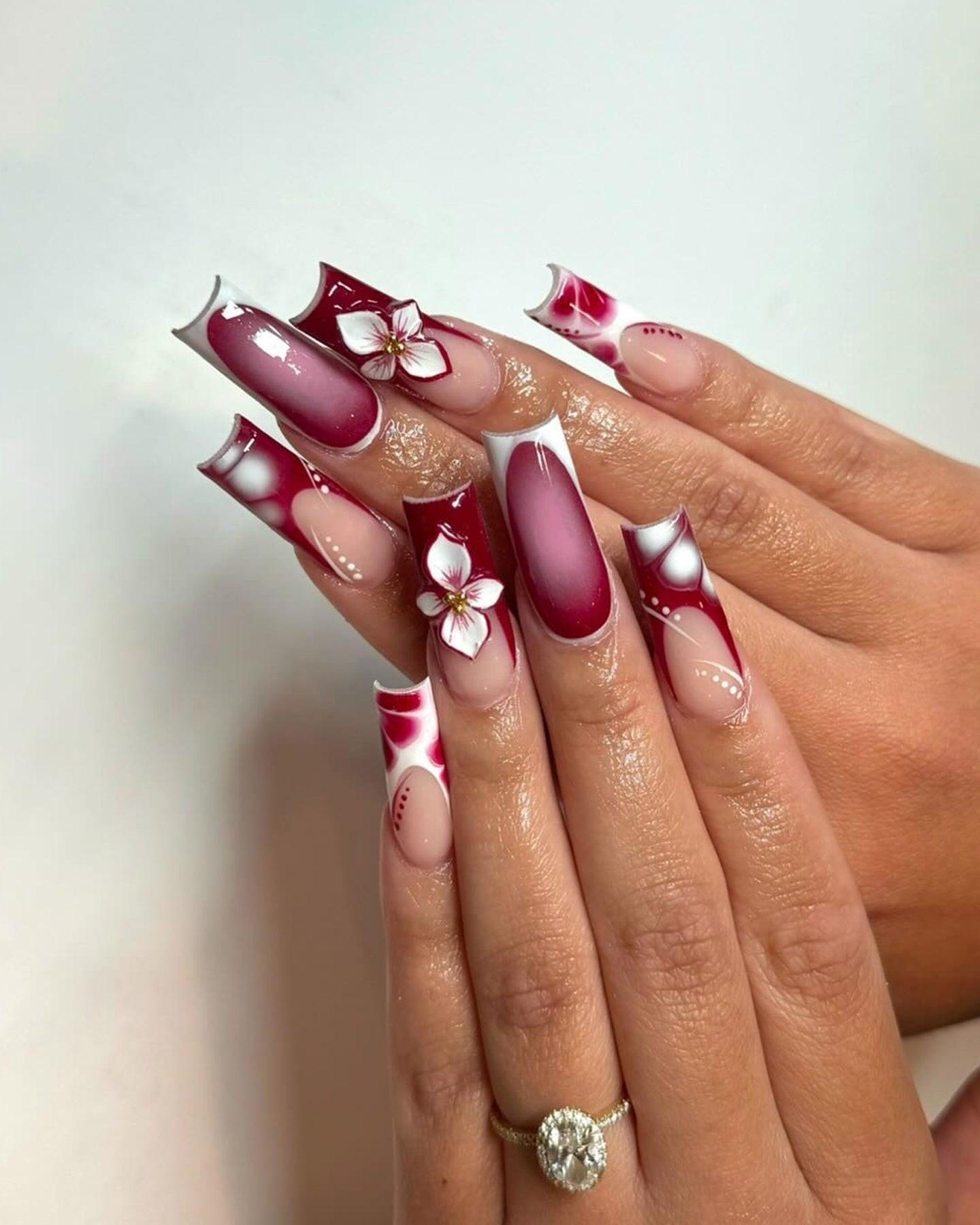 Hand with long burgundy and pink custom press-on nails featuring floral designs