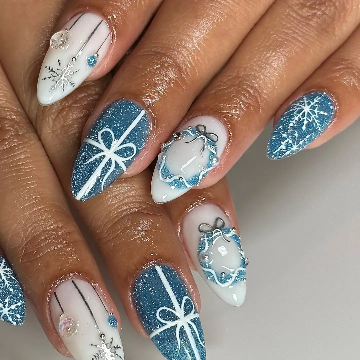 Winter-themed press-on nails with blue glitter, snowflakes, ribbon and wreath designs