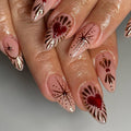 Hand with almond-shaped nude press-on nails featuring red hearts and gold starburst designs