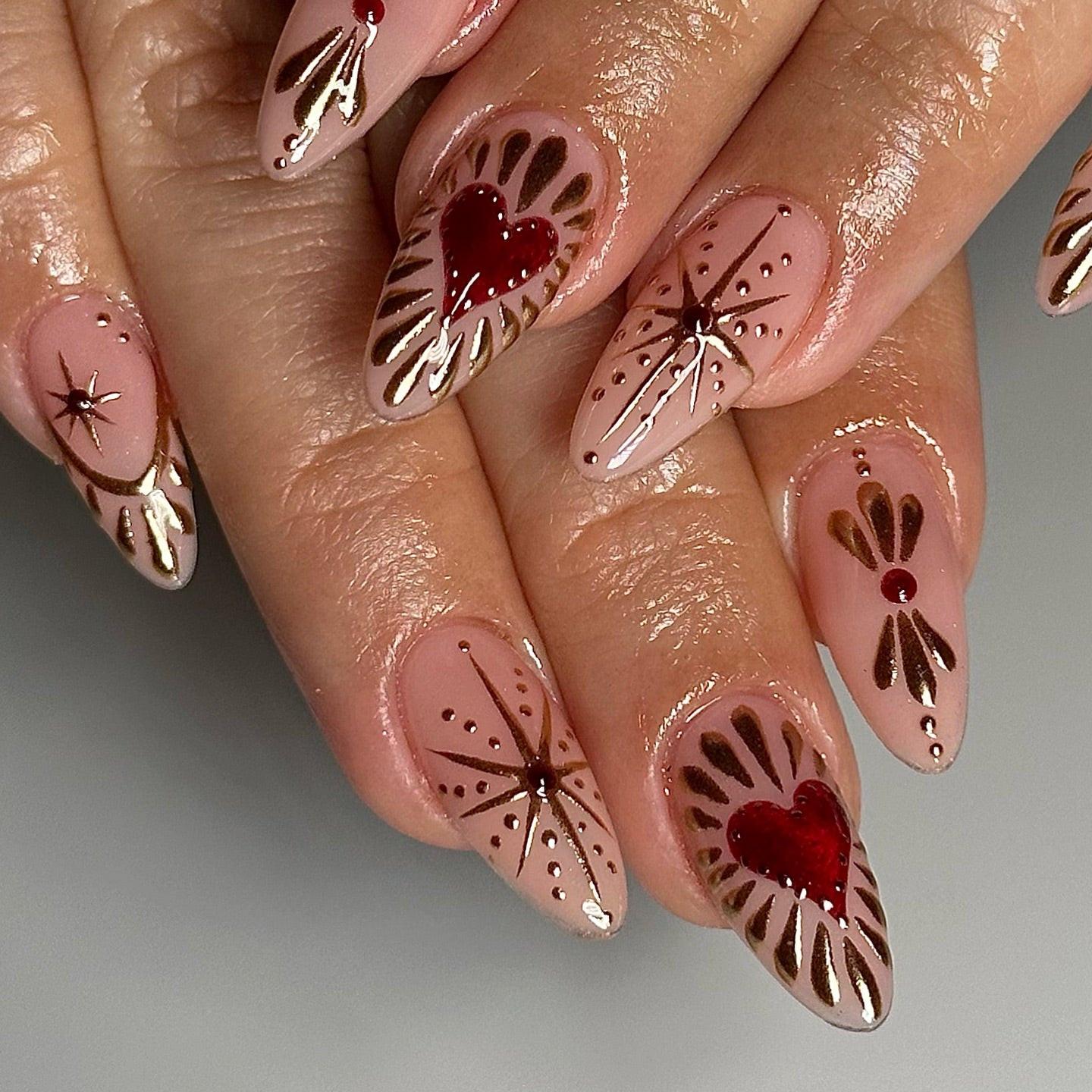 Hand with almond-shaped nude press-on nails featuring red hearts and gold starburst designs