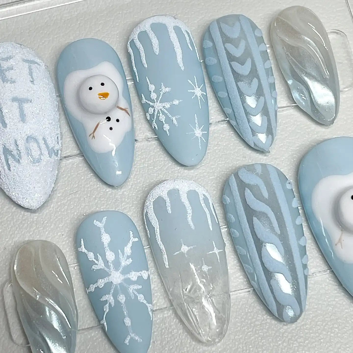 Handmade press-on nails with winter designs, snowflakes, snowmen, and blue sweater patterns