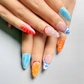 Hand with colorful press-on nails featuring orange slices, blue tips, and floral designs
