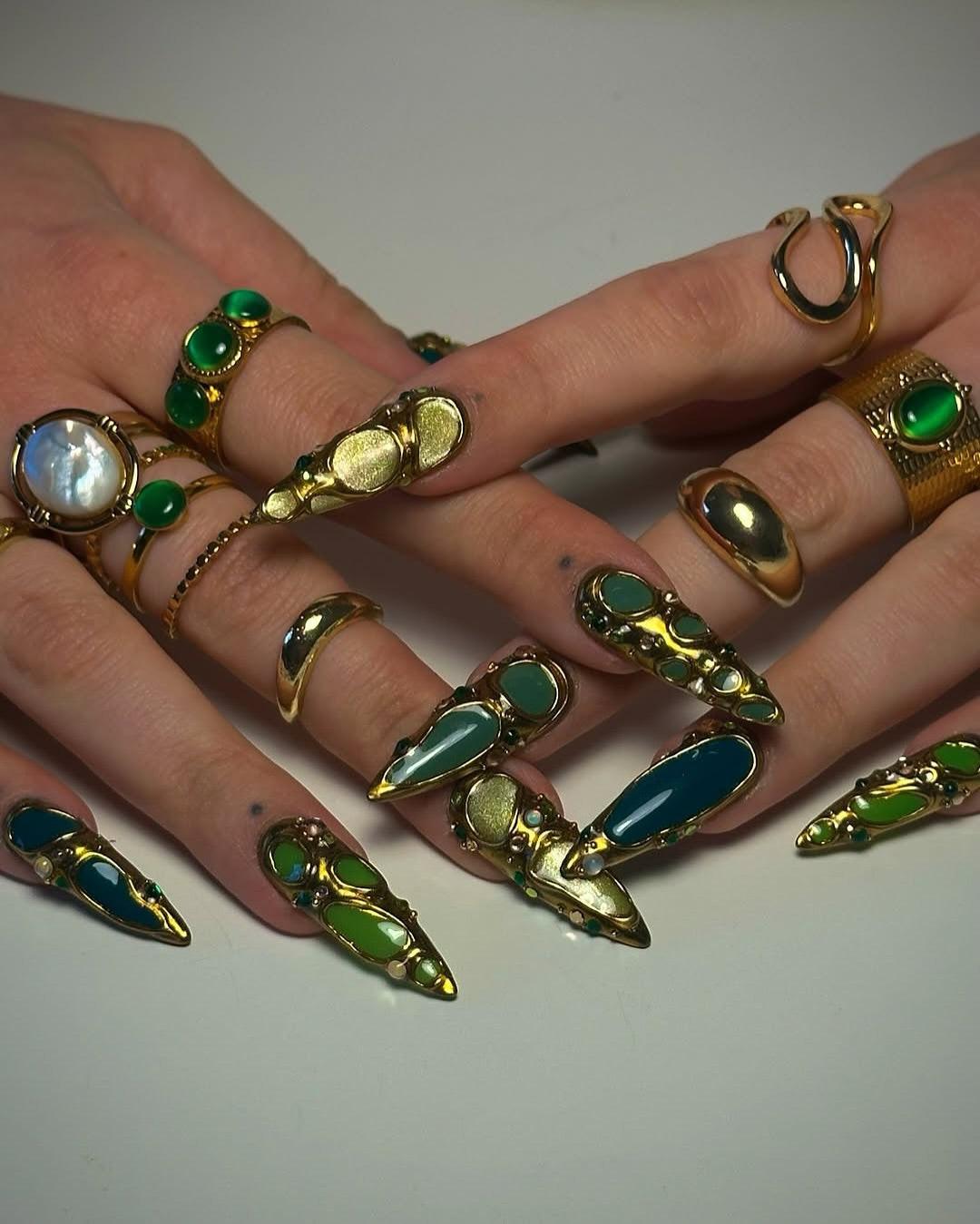Hands with handmade press-on nails in green and gold with gemstone rings, elegant nail art
