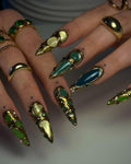 Hand with long, custom press-on nails featuring gold and green gemstone designs