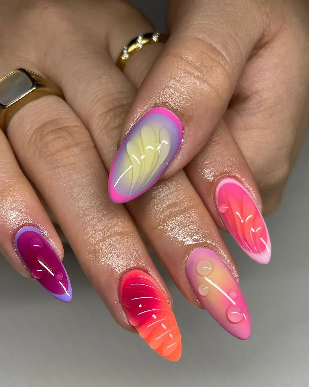 Hand with vibrant, colorful handmade press-on nails featuring gradient pink, purple, and orange designs with glossy, 3D accents.