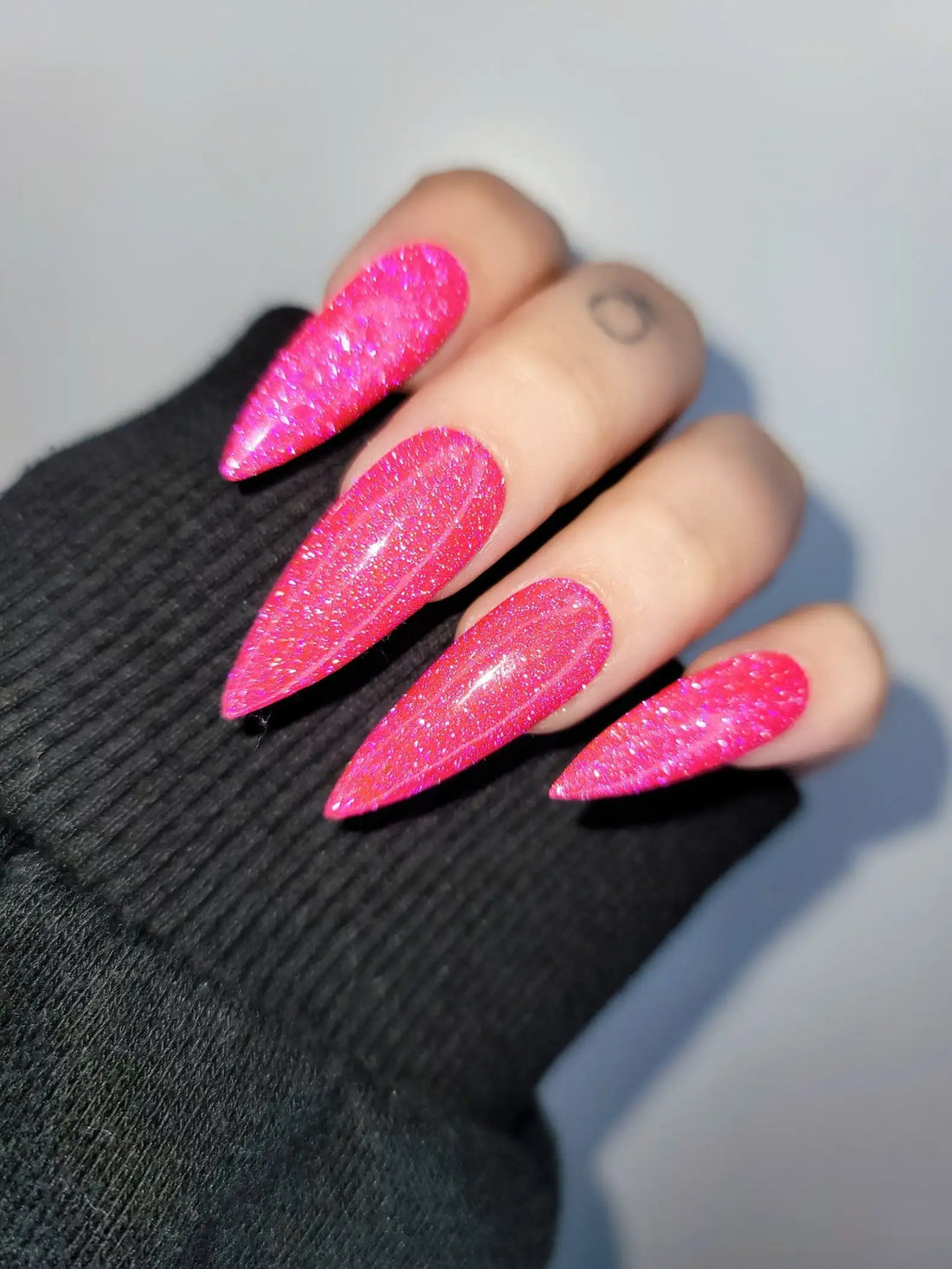Hand wearing long stiletto hot pink glitter press-on nails, close-up view