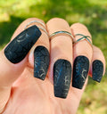 Hand with long black press-on nails featuring spider web designs, perfect for Halloween.
