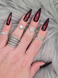 Long stiletto black and red press-on nails with glossy finish on a hand with rings, on fur