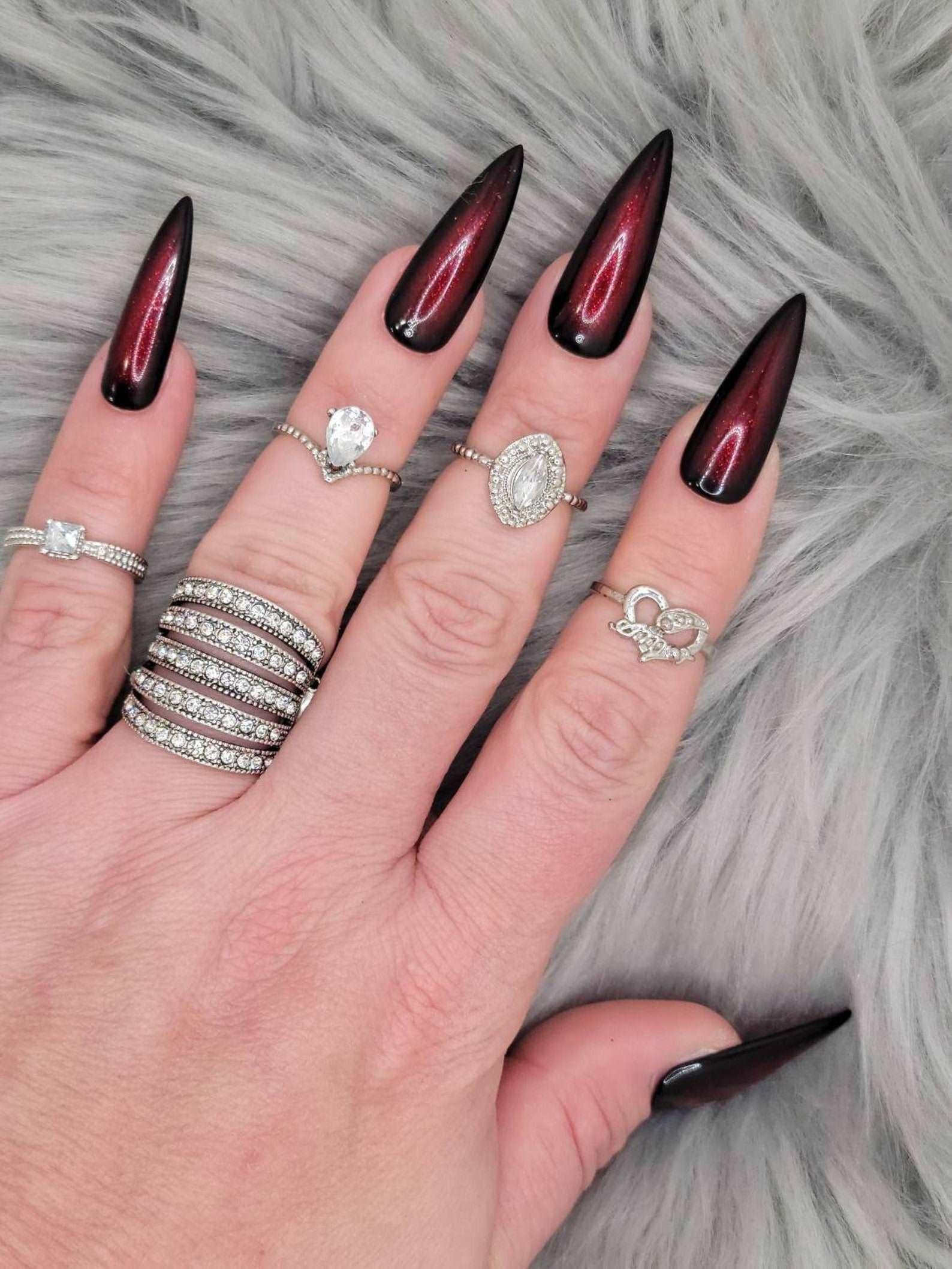 Long stiletto black and red press-on nails with glossy finish on a hand with rings, on fur