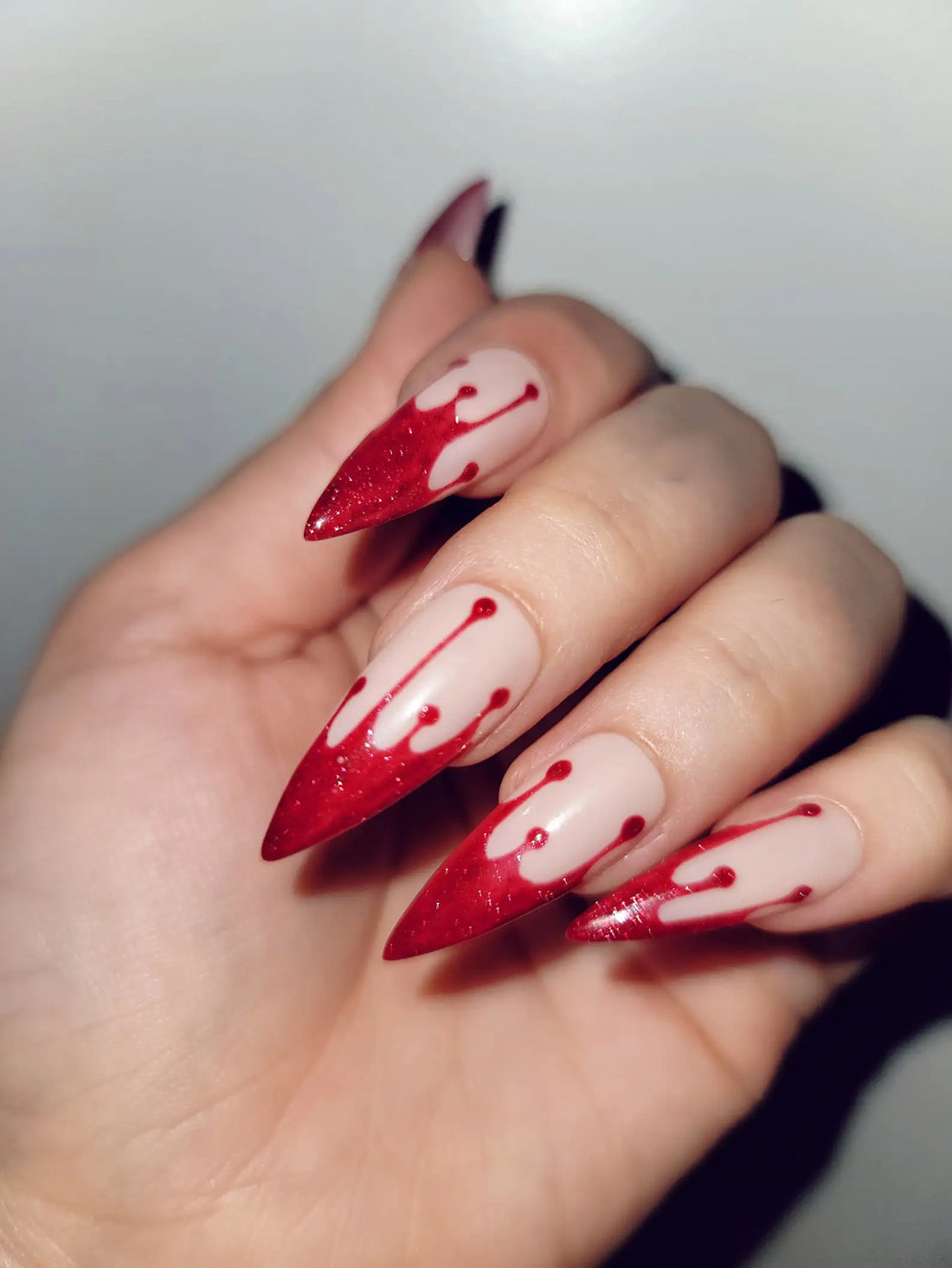 Hand with long stiletto press-on nails featuring red dripping Halloween nail art design.