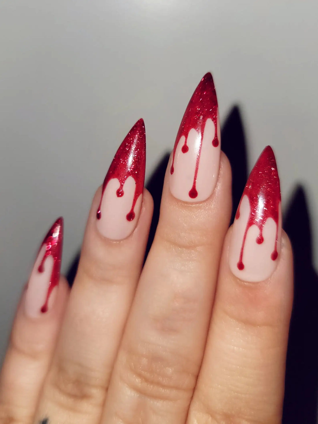 Hand with long stiletto press-on nails featuring red dripping Halloween nail art design.