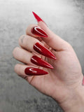 Hand with long glossy red stiletto press-on nails, close-up on gray background.