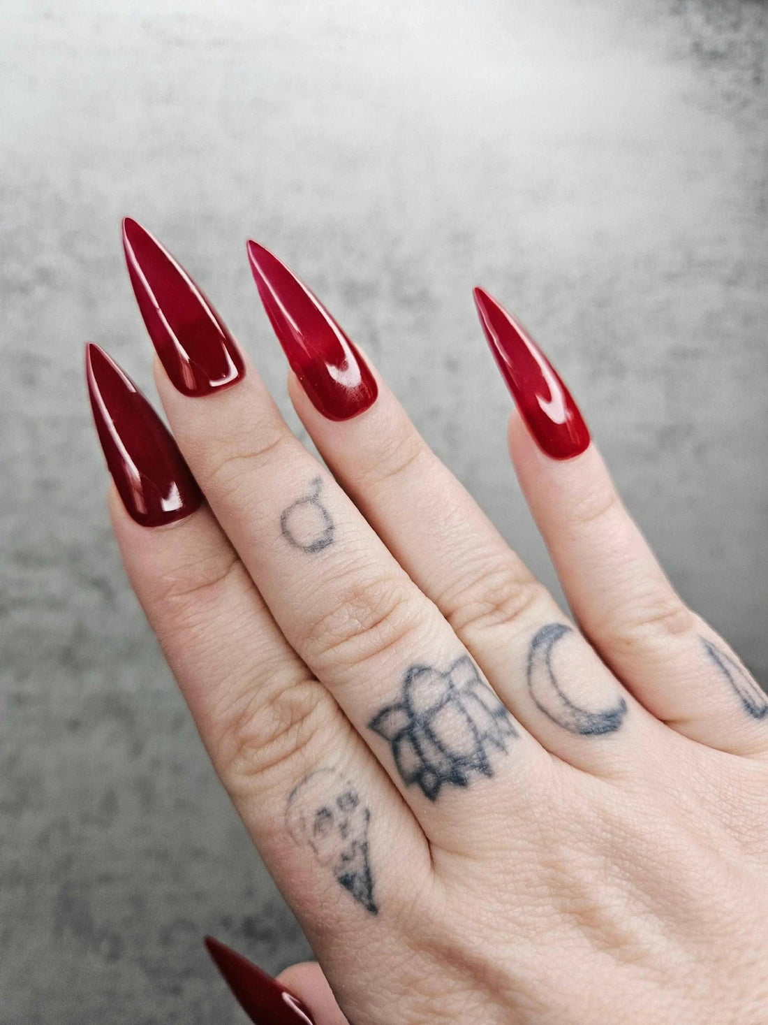 Hand with long glossy red stiletto press-on nails, close-up on gray background.