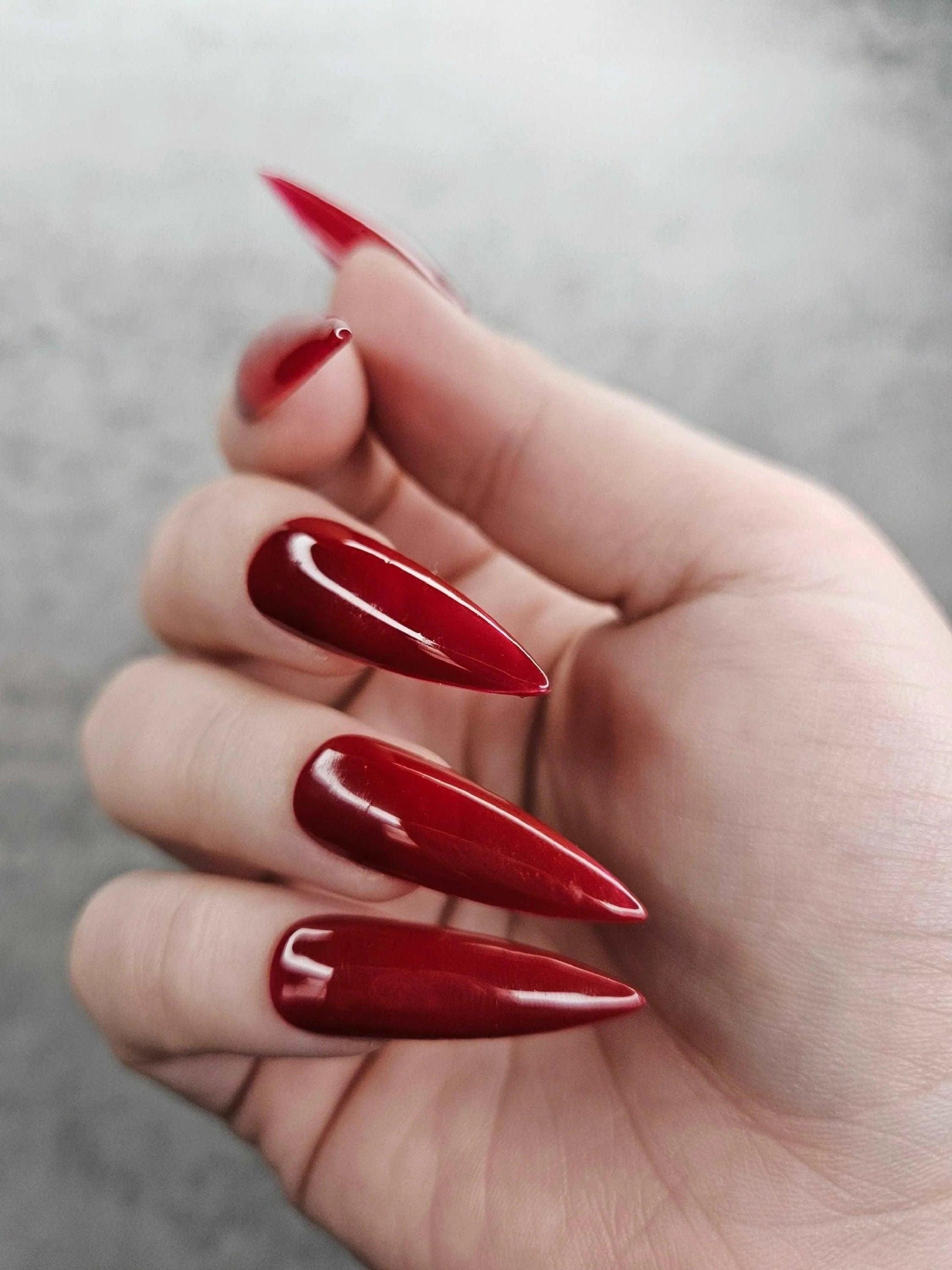 Hand with long stiletto-shaped glossy red press-on nails