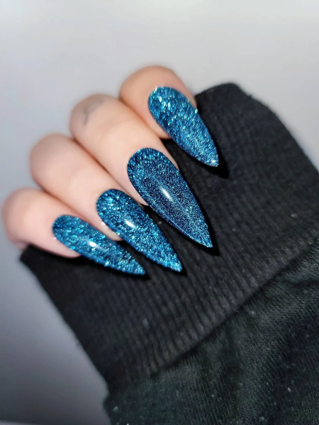 Hand with long blue glitter press-on nails in a stiletto shape
