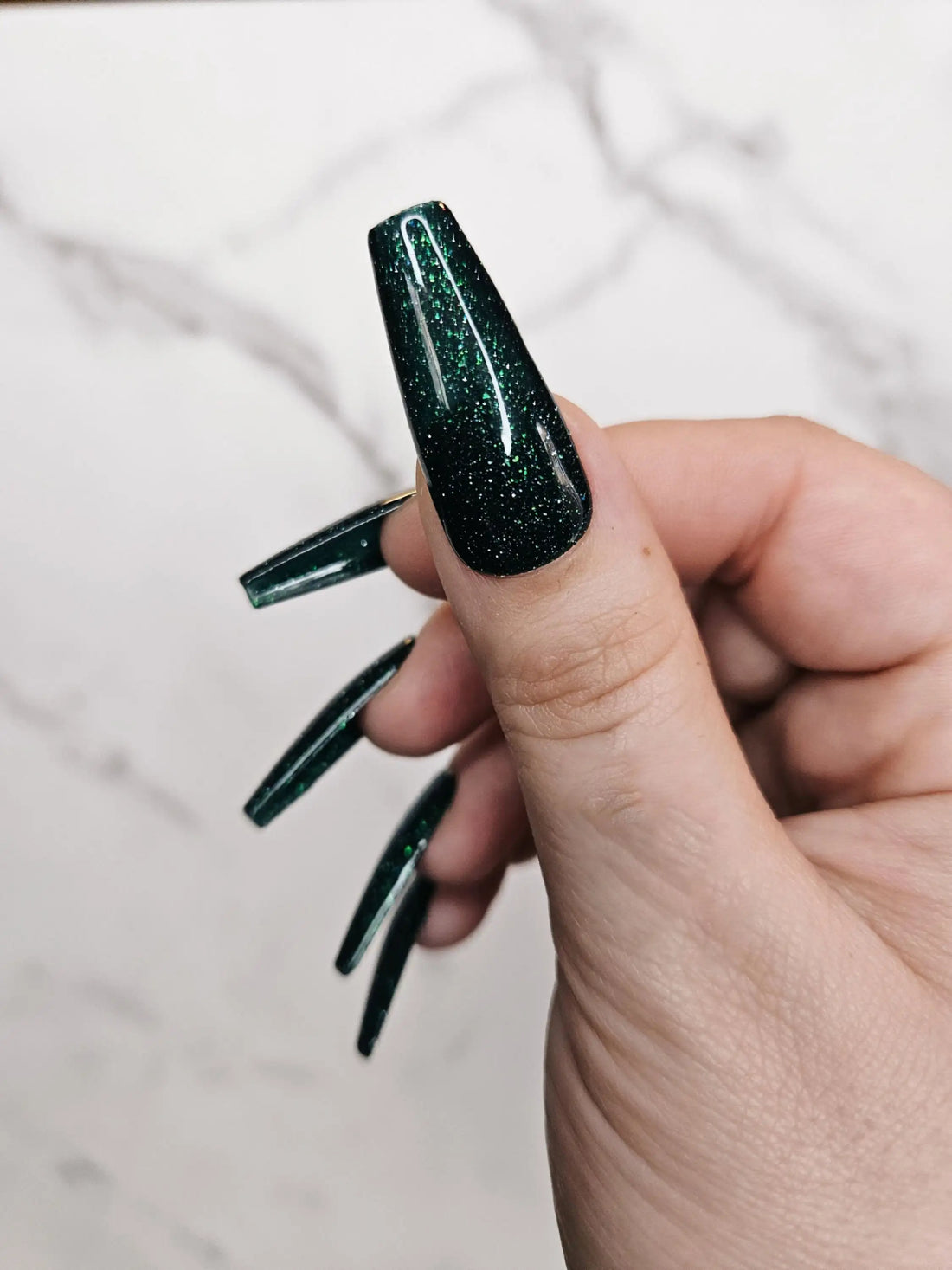Hand with long dark green glitter glossy press-on nails, almond shape, close-up