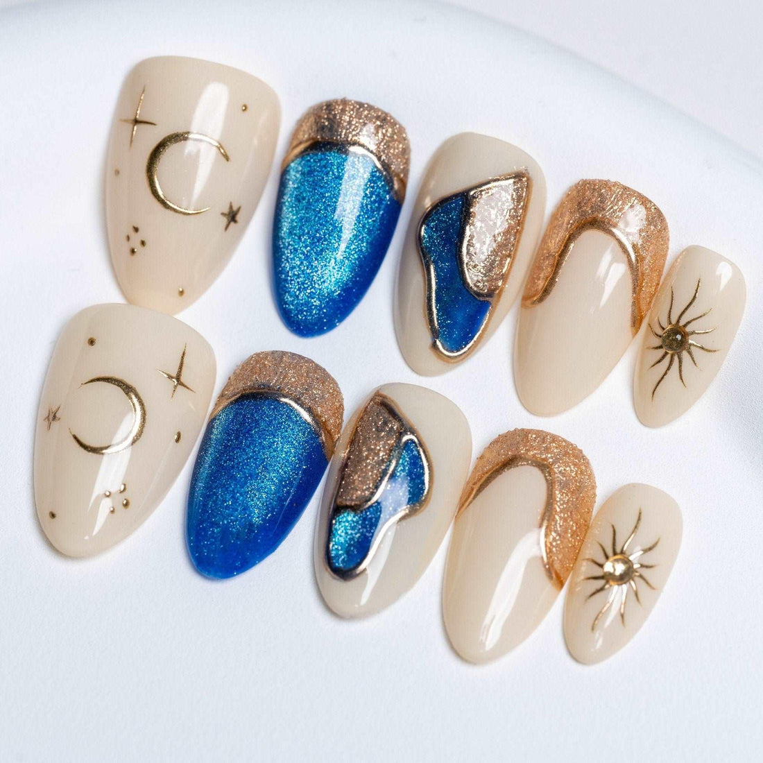 Handmade press-on nails with blue glitter, gold crescent moons, and sun designs on beige base