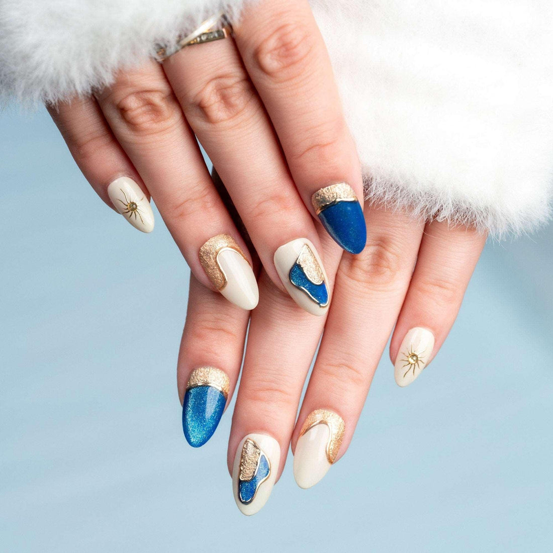 Handmade press-on nails with blue glitter, gold crescent moons, and sun designs on beige base