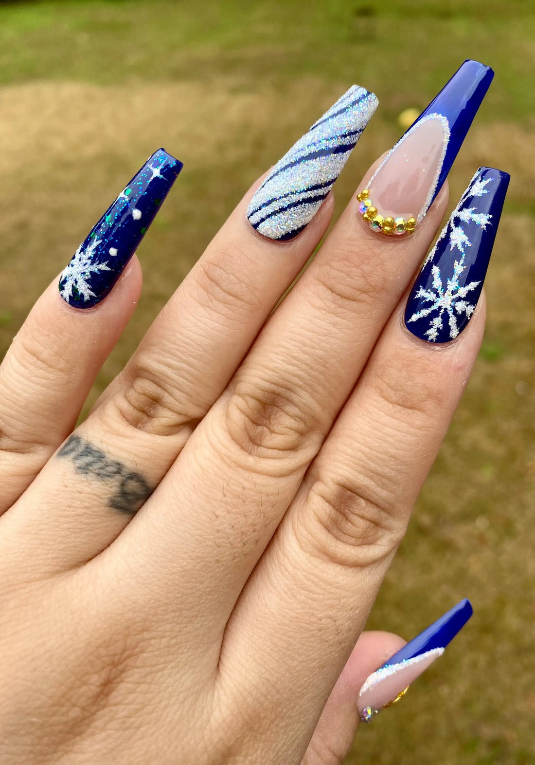 Long press-on nails with deep blue glitter, snowflake designs, silver accents, and gold gems