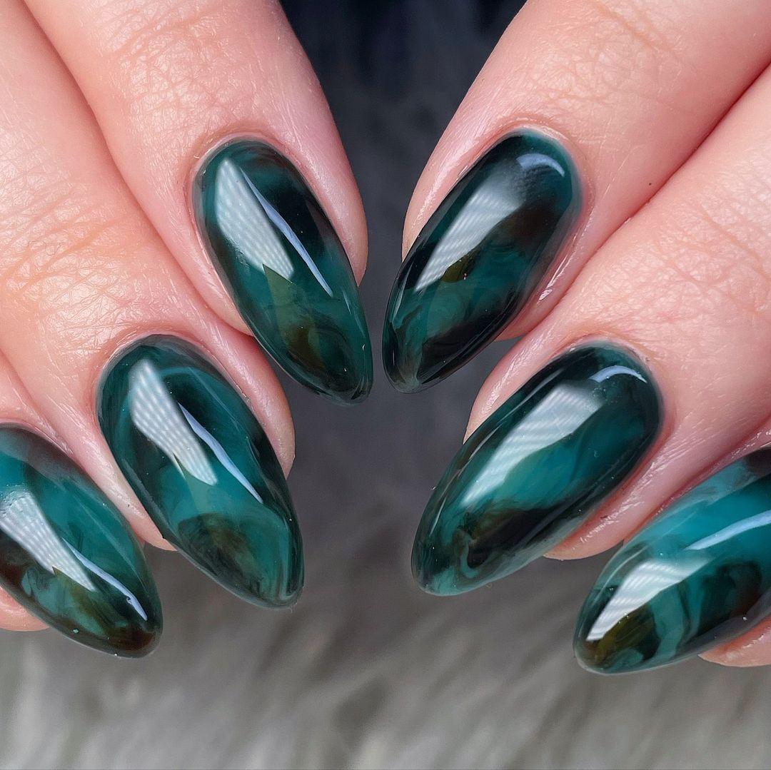 Almond-shaped deep green marble press-on nails with glossy finish on a hand