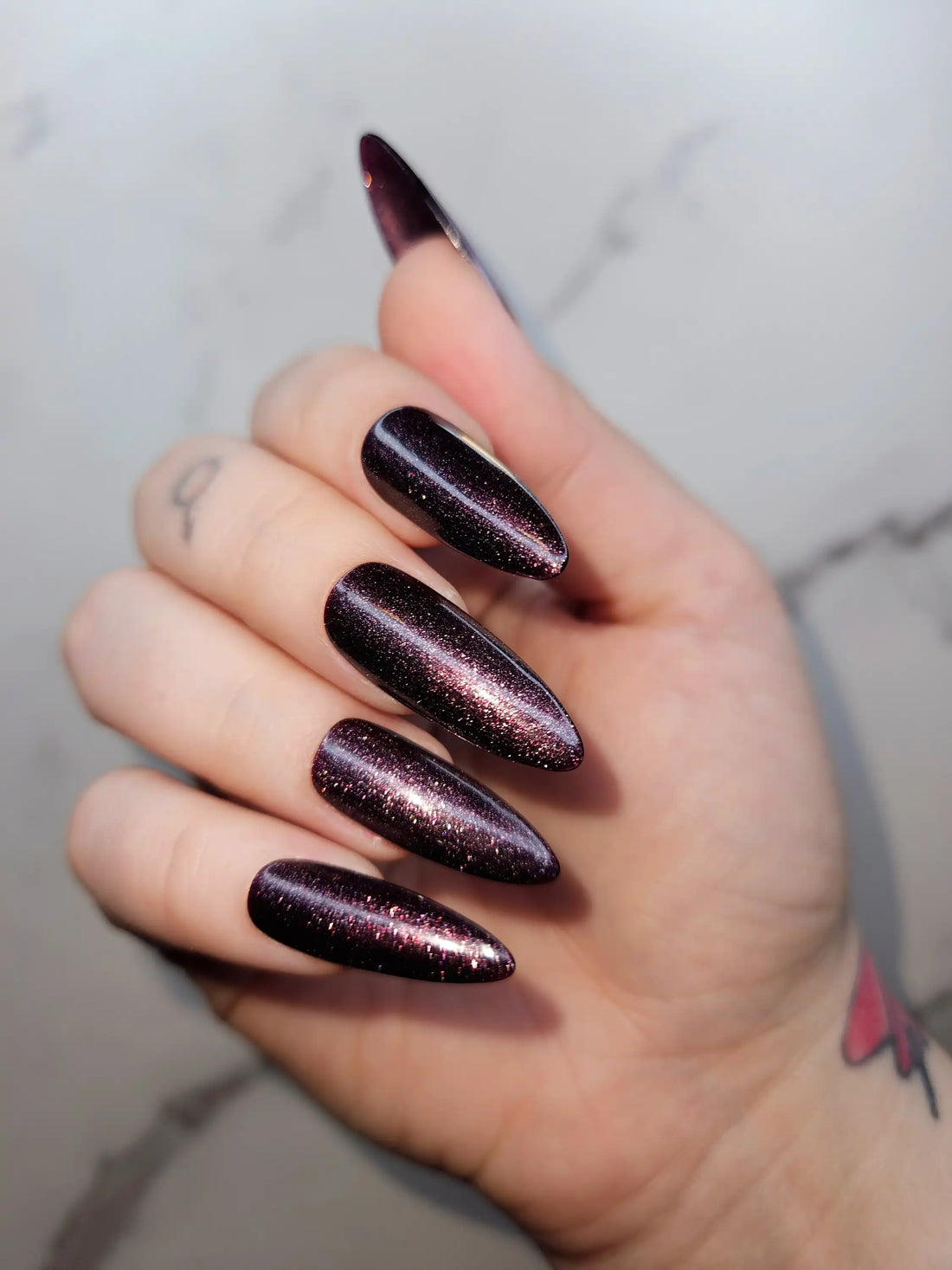 Hand with long almond-shaped dark glitter press-on nails, glossy and reusable design
