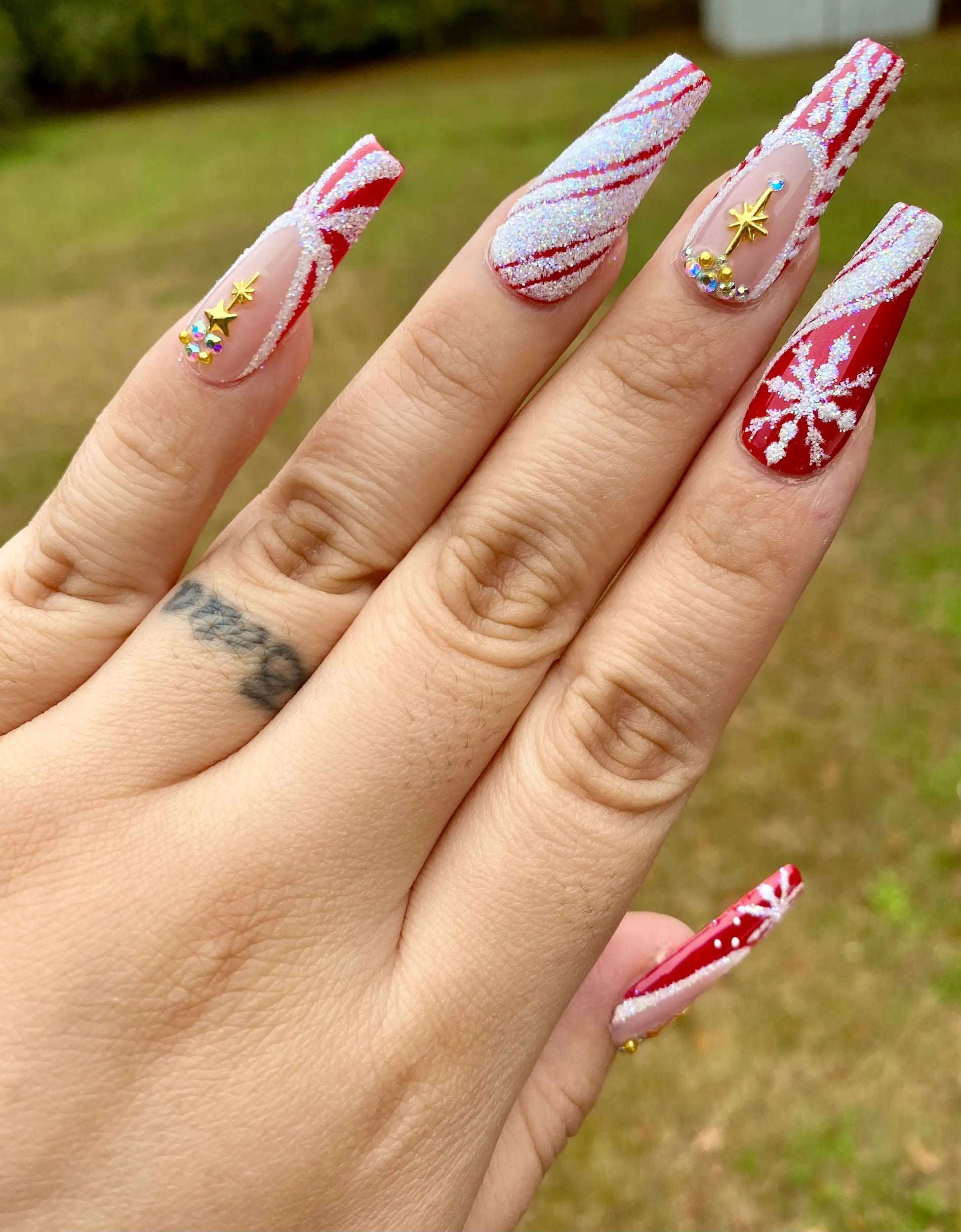 Red Christmas press-on nails with glitter snowflakes, candy cane stripes, and star rhinestones.
