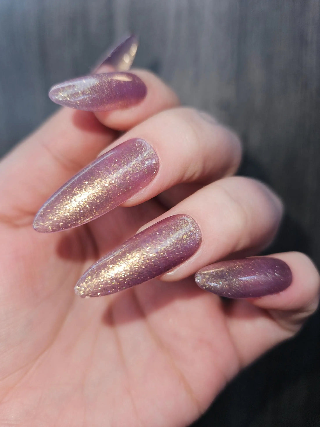 Hand with long almond-shaped purple glitter press-on nails, reusable and handmade