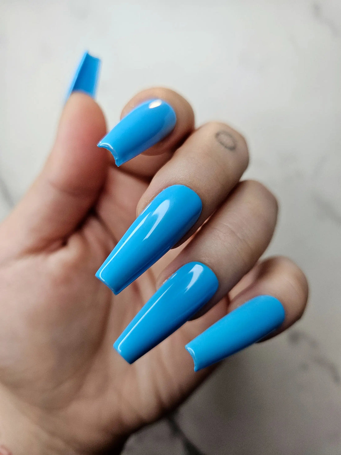 Hand with glossy blue coffin-shaped press-on nails against a light background