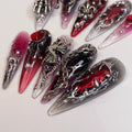 Red and black stiletto press-on nails with silver gothic cross charms and 3D metallic accents.
