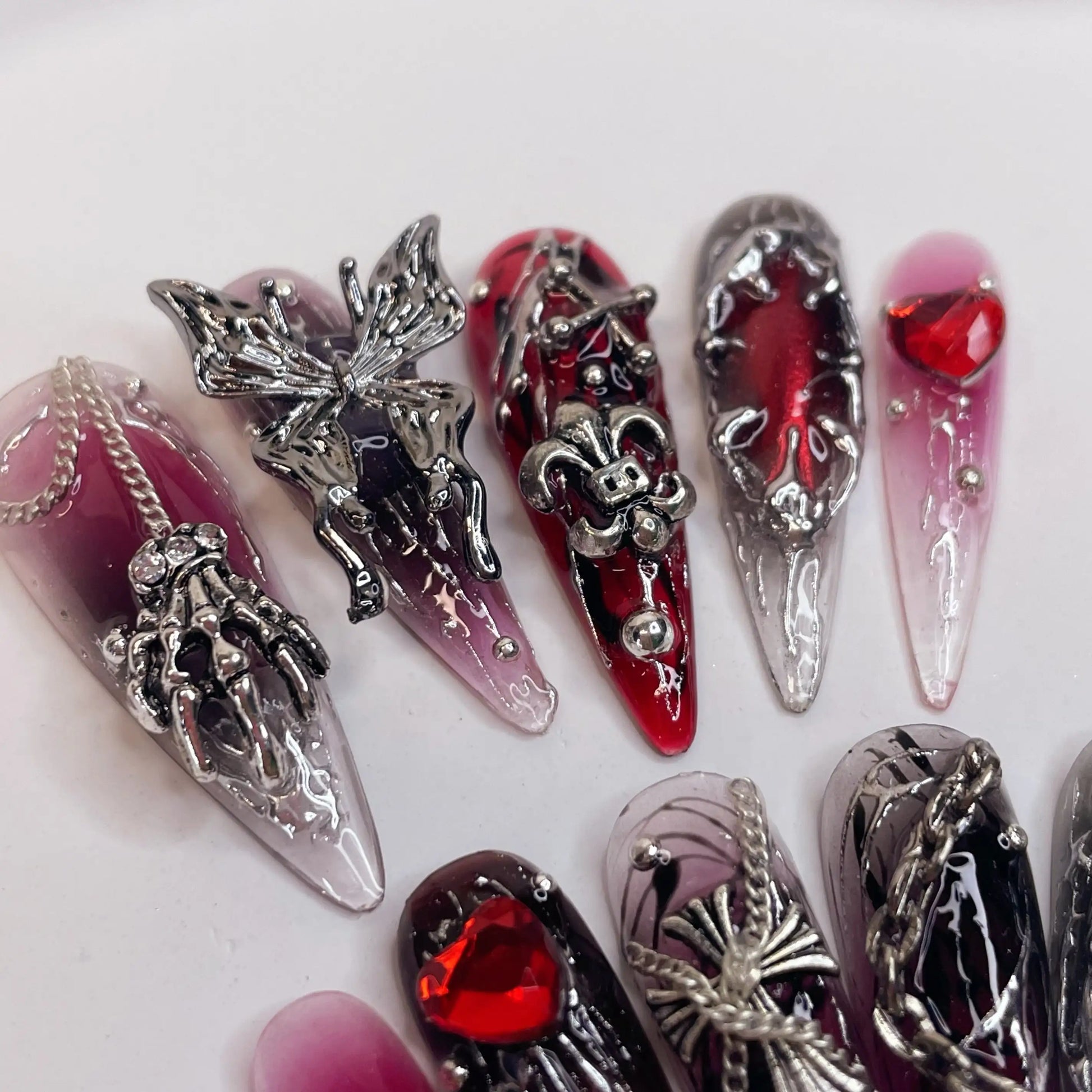 Gothic press-on nails with silver charms, red and black designs, skeleton and heart accents