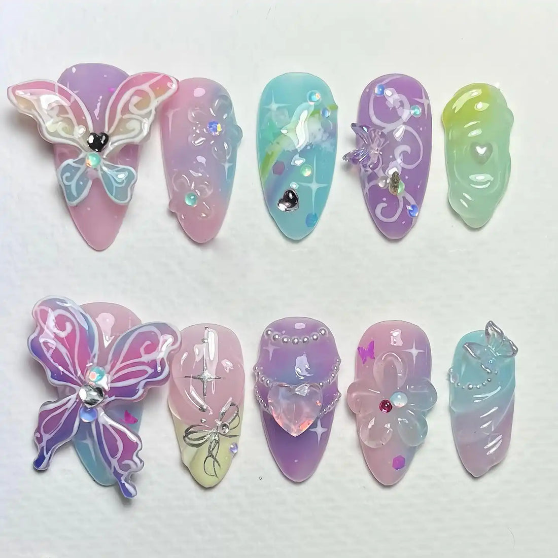 Handmade pastel ombre press-on nails with 3D butterfly, jewel, and floral designs.