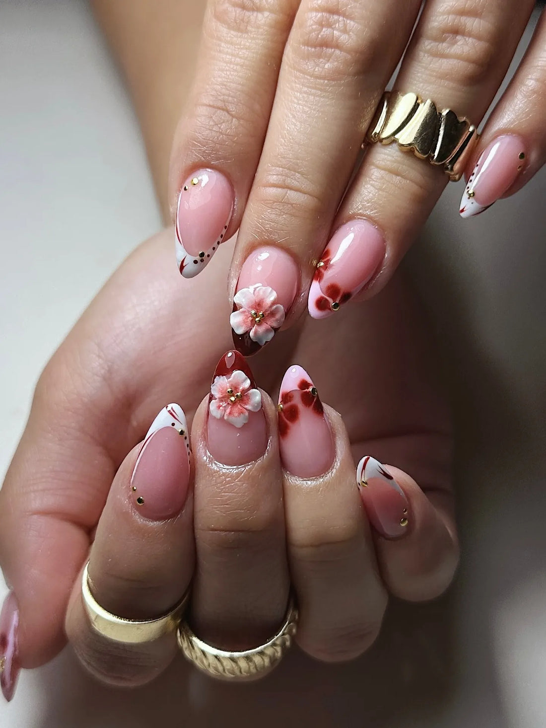 Hand with handmade 3D cherry blossom press-on nails, red floral French tips, gold beads.