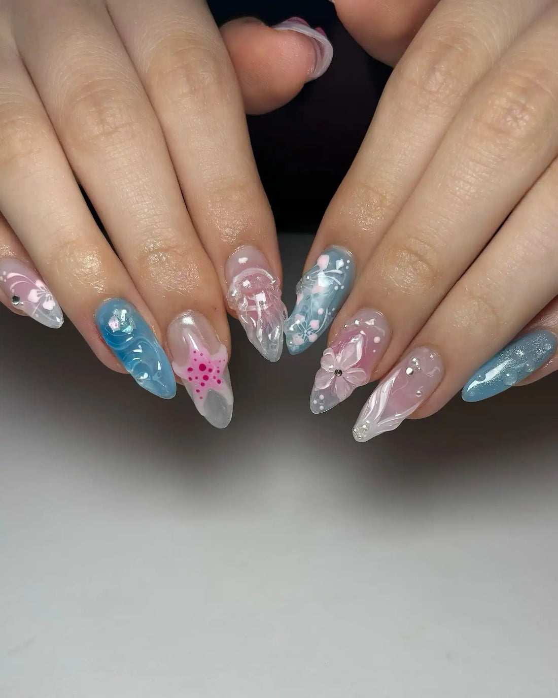 Handmade 3D floral and seashell press-on nails in pastel blue and pink with gemstone accents