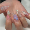 Hand with long stiletto press-on nails featuring 3D floral and butterfly designs